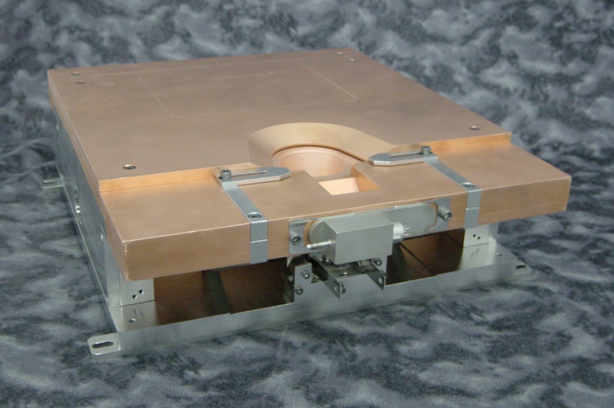 EB12 full-production electron-beam source: low-profile copper top plate with a central hearth well and clamp straps, on its support frame.